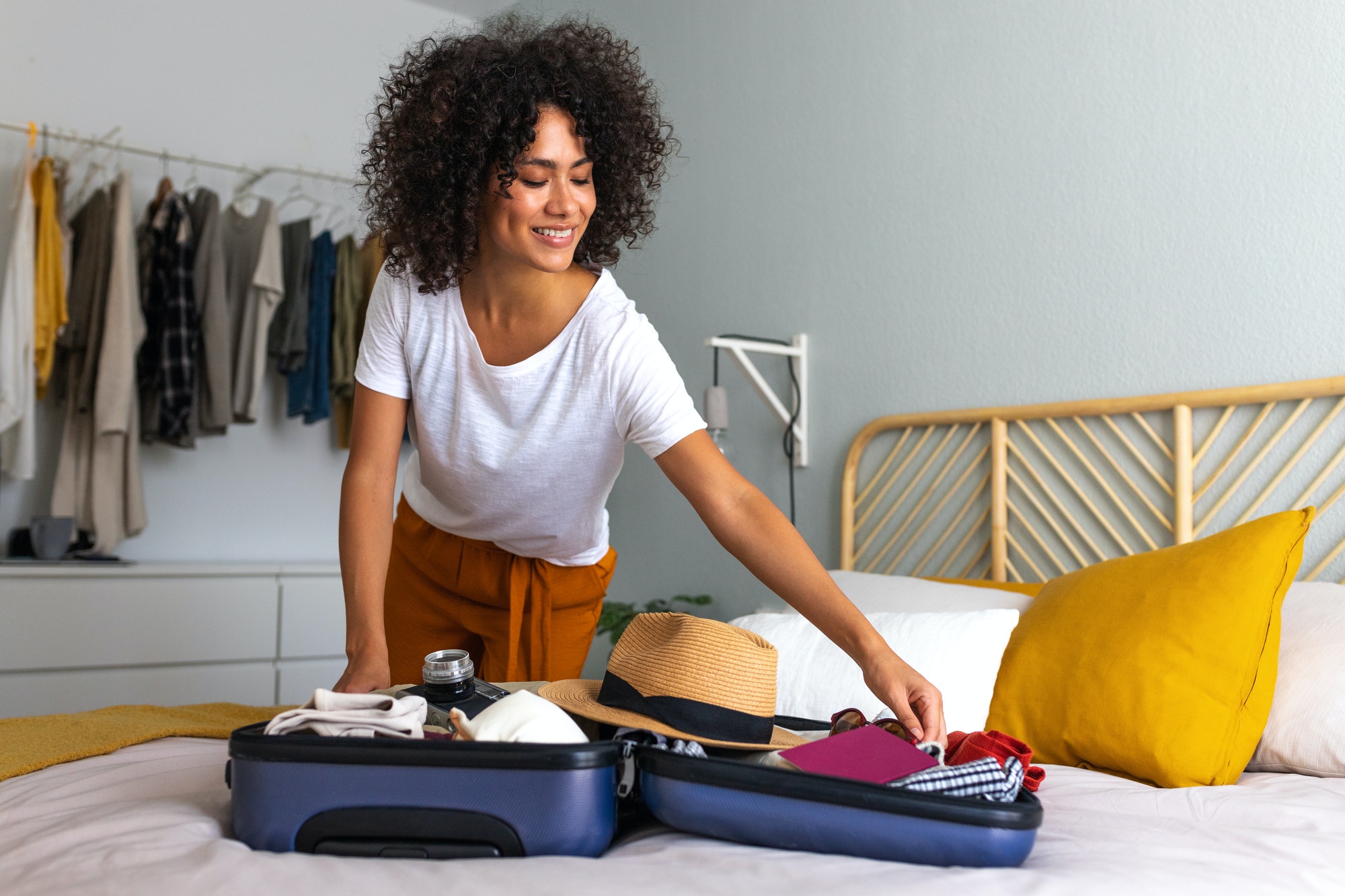 Happy African American young woman packing suitcase at home. Preparing for summer holidays abroad.