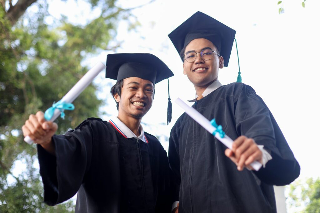 Two young Asian college graduates holding diplomas